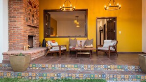 A patio with a brick fireplace, a large mirror, and three chairs with cushions. - Charming Villa Terrace Outdoor Fireplace (Jiquilpan de Juárez)