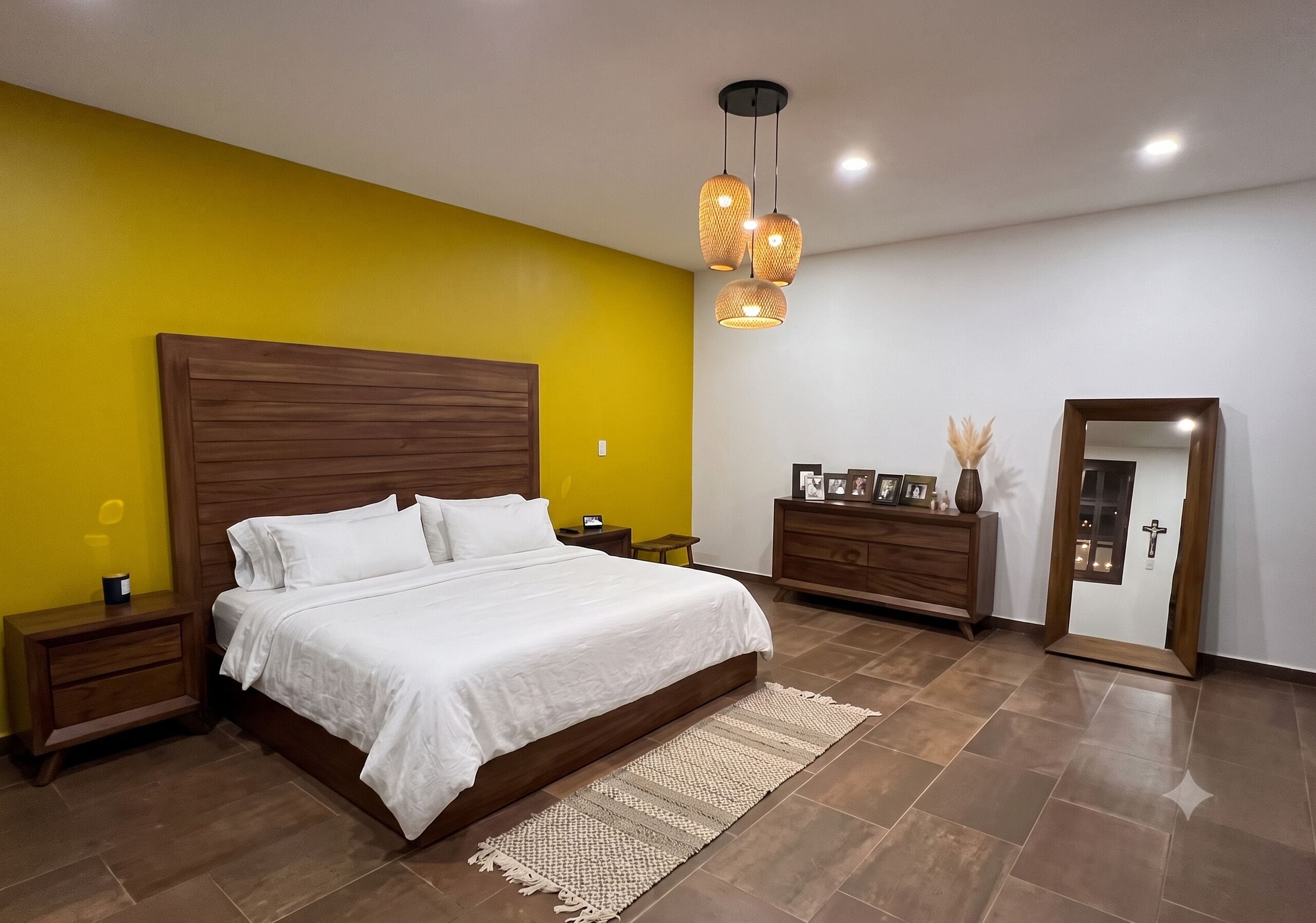 Une chambre à coucher avec un lit doté d’une tête de lit en bois, une table de chevet, une commode, un miroir et un luminaire suspendu.