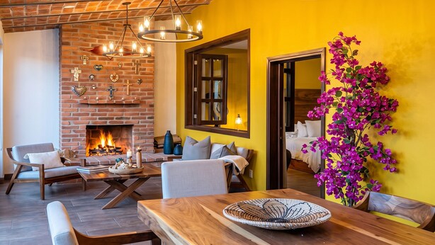 A cozy living room with a brick fireplace, modern furniture, and a vibrant yellow wall. - Charming Villa Terrace Outdoor Fireplace (Jiquilpan de Juárez)