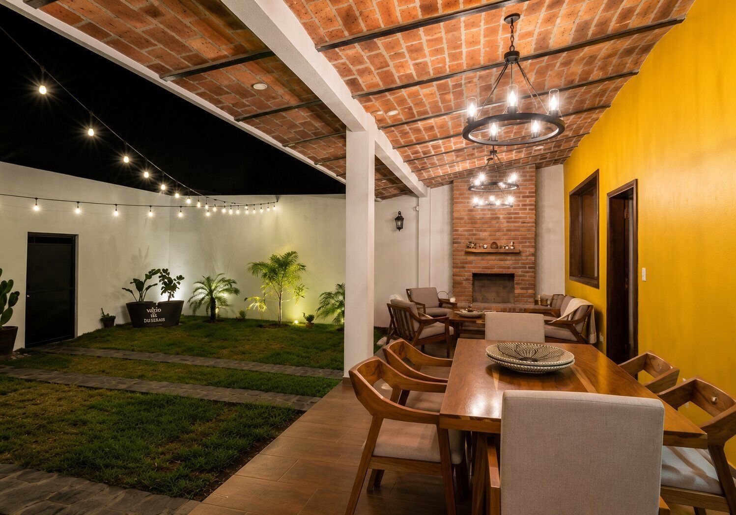 A dining area with a brick fireplace, outdoor seating, and string lights.