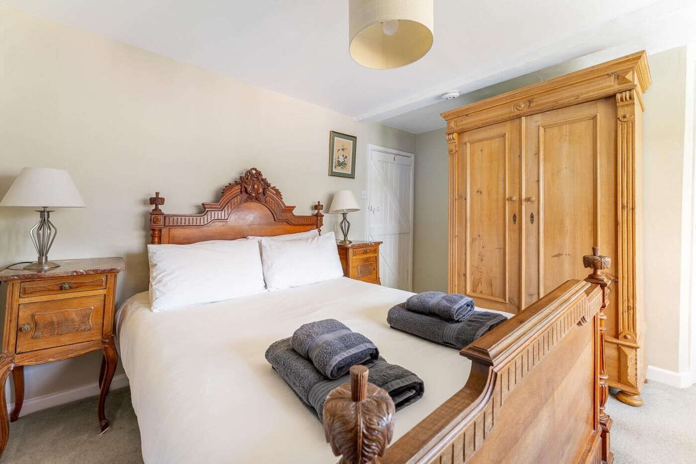A bedroom with a wooden bed, two nightstands, a wardrobe, and a hanging lamp.