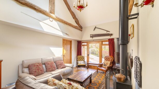 A cozy living room with a sofa, armchairs, a fireplace, and a large window. - 4 Bed in Hawkshead (oc-lr116) (Hawkshead)
