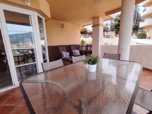 A glass-top table with a potted plant, cushioned seating, and a sliding glass door leading to a patio area. - Piso de Lujo Cerca P. Banús - Vistas mar y montaña (Marbella)