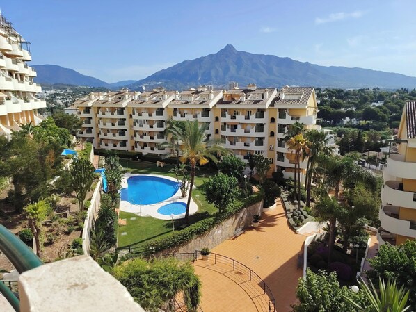 A hotel with multiple floors, a swimming pool, and a mountainous backdrop. - Piso de Lujo Cerca P. Banús - Vistas mar y montaña (Marbella)