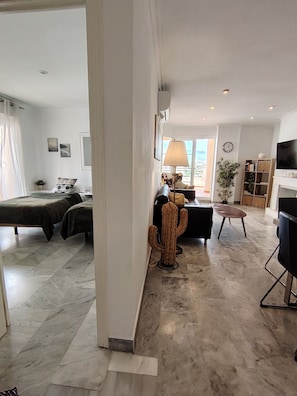 A spacious living area with a bed, a desk, a chair, a lamp, a cactus, a television, and a bookshelf. - Piso de Lujo Cerca P. Banús - Vistas mar y montaña (Marbella)