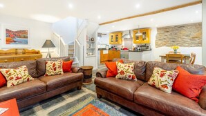 A living room with two brown leather sofas, a patterned rug, and a kitchen in the background. - 3 Bed in Ambleside (oc-lr133) (Ambleside)