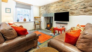 A cozy living room with leather sofas, a stone wall, a fireplace, and a flat-screen TV. - 3 Bed in Ambleside (oc-lr133) (Ambleside)