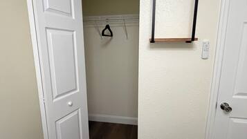 A hallway with a white door, a coat rack, a shelf with a remote, and a wooden floor.