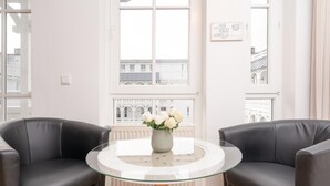 A room with two black leather sofas, a glass table with a vase of white flowers, and large windows with a view of buildings. - Moderne Strandnahe Ferienwohnung in Sellin mit Balkon (Sellin)