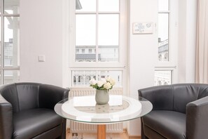 A room with two black leather sofas, a glass table with a vase of white flowers, and large windows with a view of buildings. - Moderne Strandnahe Ferienwohnung in Sellin mit Balkon (Sellin)