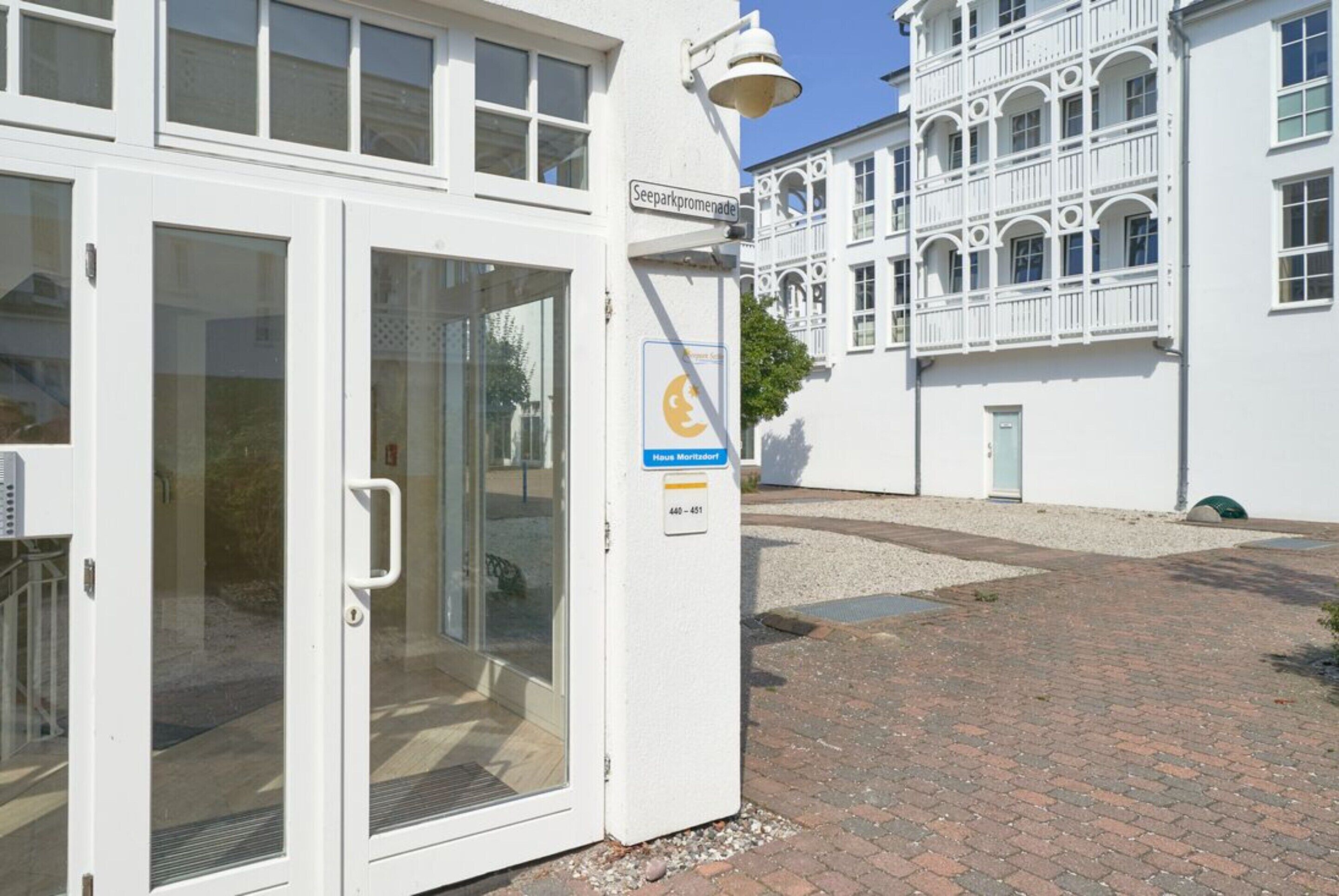 Ein weißes Gebäude mit Glastür, einer Schilder 'Seeparkpromenade' und einem blauen Schild mit einem gelben Symbol.