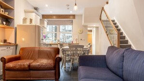 A living room with a brown leather sofa, a blue sofa, a dining area with a wooden table and chairs, and a staircase. - 3 Bed in Ambleside (oc-lr052) (Ambleside)