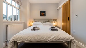A bedroom with a bed, two bedside lamps, a radiator, a window, and a door. - 3 Bed in Ambleside (oc-lr052) (Ambleside)