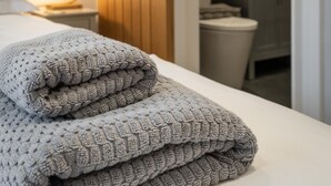 A neatly made bed with a folded blanket, a bedside lamp, and a wooden panel wall. - 3 Bed in Ambleside (oc-lr052) (Ambleside)