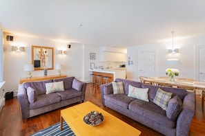 A modern living room with two sofas, a coffee table, and a kitchen in the background. - 1 Bed in Ambleside (oc-lr209) (Claife)