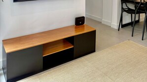Ein modernes Wohnzimmer mit einem an der Wand montierten Flachbildfernseher, einem Holzkonsolentisch und einem Essbereich mit Tisch und Stühlen.