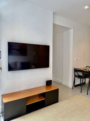 Ein modernes Wohnzimmer mit einem an der Wand montierten Flachbildfernseher, einem Holzkonsolentisch und einem Essbereich mit Tisch und Stühlen.