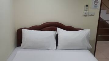 A hotel room with a bed, pillows, a wall-mounted painting, a telephone, and a no-smoking sign.