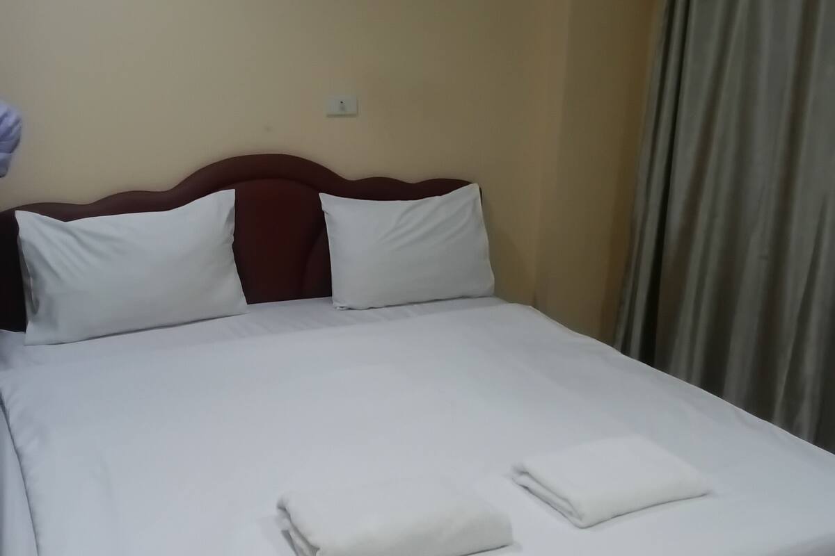 Ein ordentlich gemachtes Bett mit weißer Bettwäsche, einem Holzkopfteil und einer einzelnen Wandsteckdose.