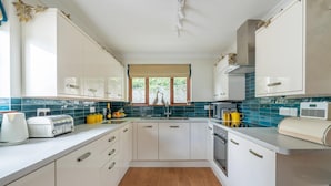 A kitchen with white cabinets, a window with a view, a sink, and a stove. - 4 Bed in Ambleside (oc-lr054) (Ambleside)