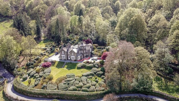 Uma casa grande e histórica cercada por jardins bem cuidados e um caminho sinuoso.