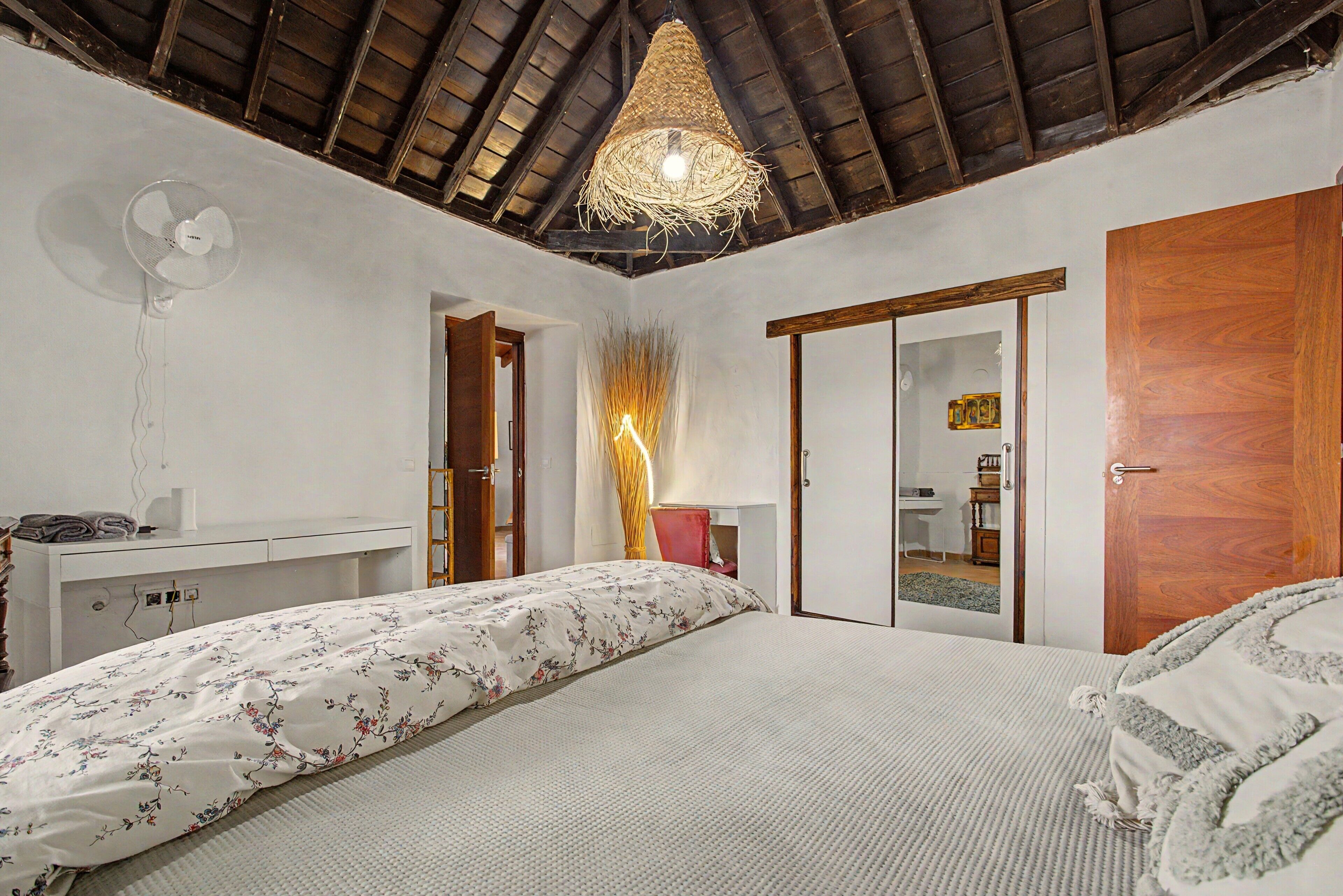 A bedroom with a bed, a desk, a wardrobe, and a ceiling fan.