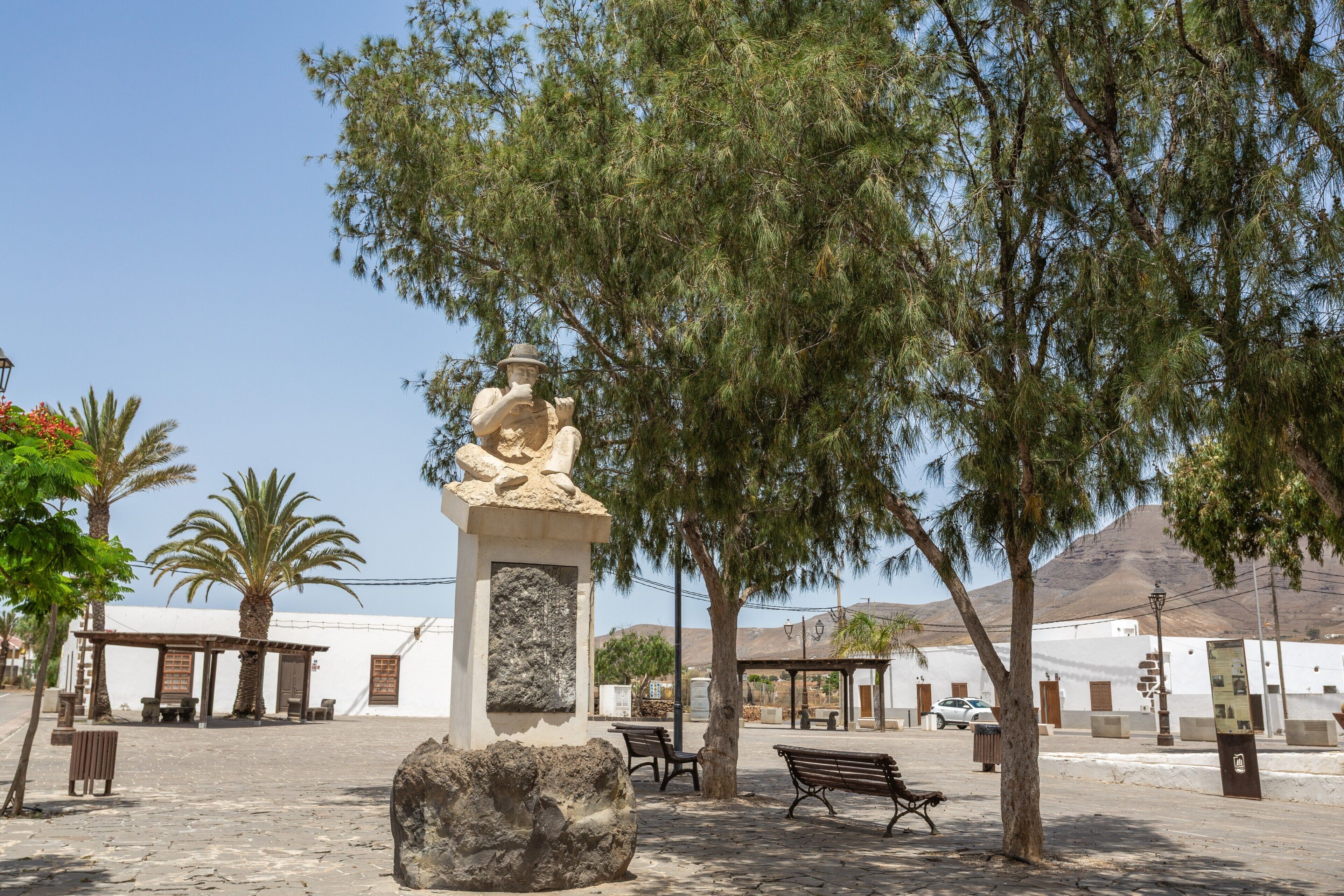 A plaza with a statue, benches, and palm trees.