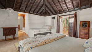 Un dormitorio con techo de madera, una cama con colcha estampada, un aparador de madera y un ventilador.