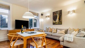 Uma sala de estar moderna com área de jantar, móveis de madeira, televisão de tela plana e um quadro na parede.