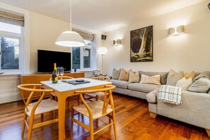 A modern living room with a dining area, wooden furniture, a flat-screen TV, and a painting on the wall. - 1 Bed in Pullwood Bay Estate (oc-lr220) (Claife)