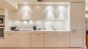 Uma cozinha moderna com armários brancos, bancada, chaleira, torradeira e pia.