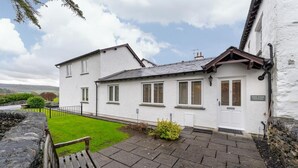 Una cabaña blanca con un camino de piedra, un banco y un letrero que dice 'Yew Tree Cottage'.
