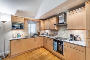A modern kitchen with wooden cabinets, a stainless steel range hood, and a built-in oven.