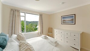 Quarto com cama, penteadeira, cadeira, janela com cortinas e um quadro na parede.