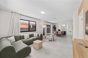 A modern living room with a sectional sofa, a coffee table, and a dining area with chairs and a table. - Central Miami Home • Near Airport & Coral Gables (Miami)