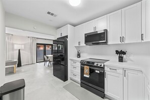 A modern kitchen with white cabinets, a black stove, a microwave, and a refrigerator. - Central Miami Home • Near Airport & Coral Gables (Miami)