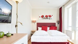 Hotellihuone, jossa on sänky, yöpöydät, televisio ja taulu seinällä.