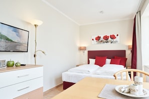 Une chambre d’hôtel avec un lit, des lampes de chevet, une télévision, un bureau avec une radio et un tableau au mur.