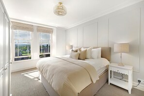 Ein Schlafzimmer mit einem großen Bett, einem Nachttisch, einer Lampe und Blick ins Freie durch ein Fenster.