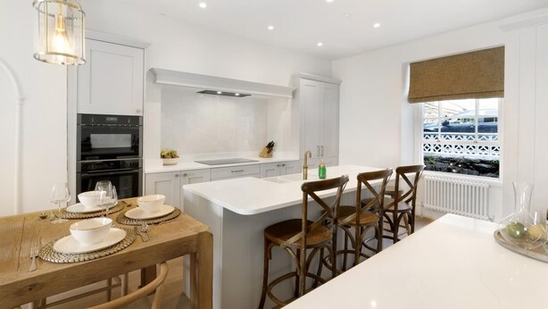 A modern kitchen with white cabinetry, a central island, and a dining area with wooden chairs. - 4 Bed in Windermere (oc-lr186) (Windermere)