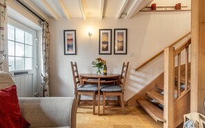 A dining area with a wooden table and chairs, a vase with flowers, and framed pictures on the wall. - 1 Bed in Ambleside (oc-lr167) (Ambleside)