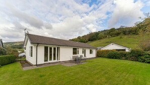 Ein eingeschossiges Haus mit einem Ziegeldach, einer einladenden Veranda mit Tisch und Stühlen und einem gepflegten Rasen.