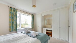 Ein Schlafzimmer mit Bett, Kommode, Spiegel und einem Fenster mit Vorhängen.