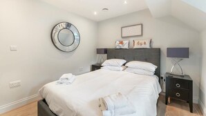 Un dormitorio moderno con cama, mesitas de noche, un espejo redondo y un cuadro en la pared.