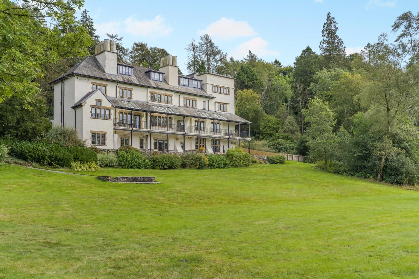 A large, multi-story building with a symmetrical facade, surrounded by a well-maintained lawn and dense trees.
