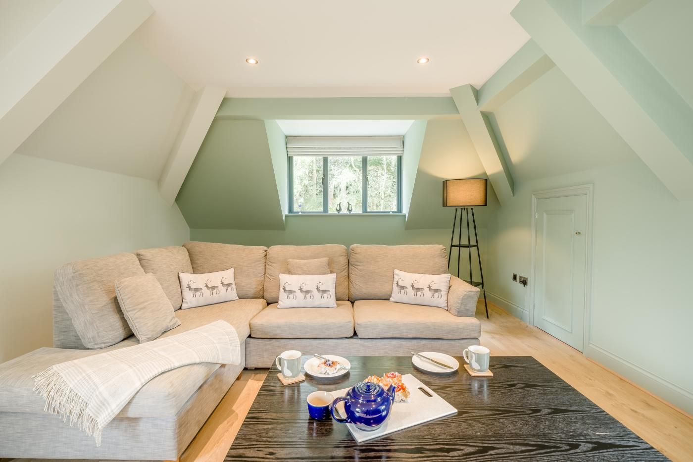 A modern living room with a sectional sofa, a coffee table with a tray of food and drinks, and a lamp.