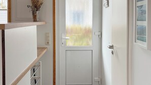 En gang med en sandblæst glasdør, en lille hylde med tørrede planter og et gråt tæppegulv.