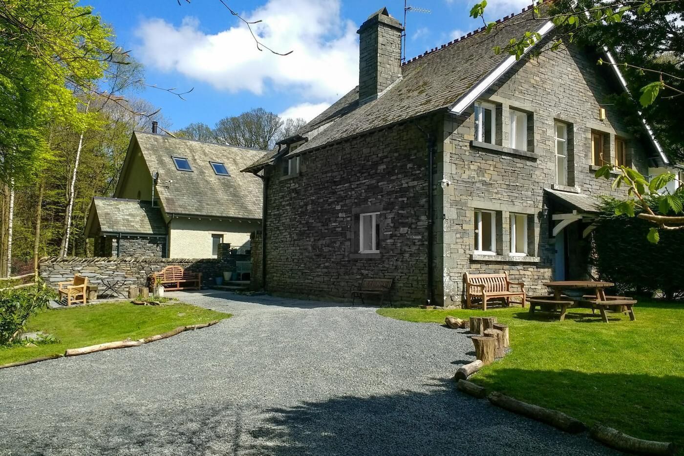 A stone building with a gravel driveway, wooden benches, and a picnic table.