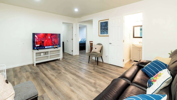 A living room with a flat-screen TV, a leather sofa, and a wooden floor. - Foothills LA Family Friendly House (Glendora)