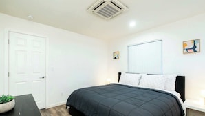 A bedroom with a black bedspread, white walls, a white door, and a window with blinds. - Foothills LA Family Friendly House (Glendora)